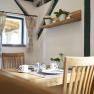 A cozy breakfast room with a wooden table, chairs and decorative plants on a shelf.