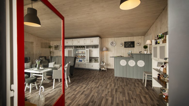 Innenansicht eines gemütlichen Cafés mit Holzboden, weißen Möbeln und dekorativen Elementen.