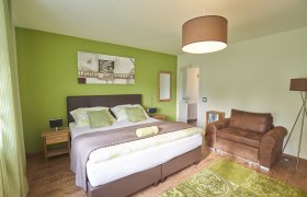 Modern eingerichtetes Gästezimmer mit grünem Akzent, Doppelbett, braunem Sessel und dekorativem Bild an der Wand.