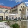 Großes gelbes Gebäude mit roten Dachziegeln, Springbrunnen und Pavillon im Vordergrund.