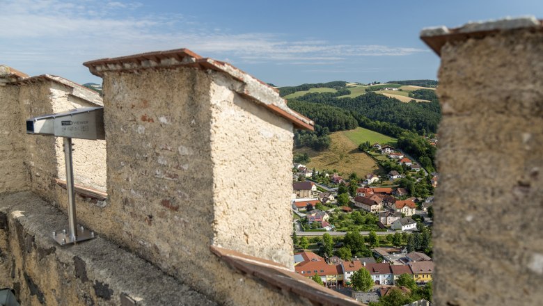 Aussicht von einer Burgruine auf eine Stadt und grüne Hügel.