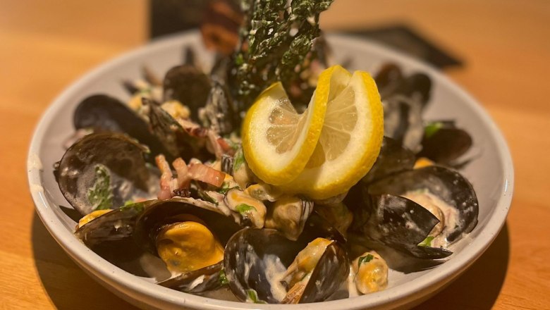 A plate with mussels, cream sauce and lemon slices on a wooden table.