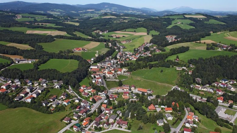 Luftaufnahme von Zöbern, einer ländlichen Gemeinde mit Häusern und Feldern, umgeben von Hügeln und Wäldern.