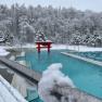 Ein verschneites Außenbecken einer Therme mit roten asiatischen Elementen und schneebedeckten Bäumen im Hintergrund.