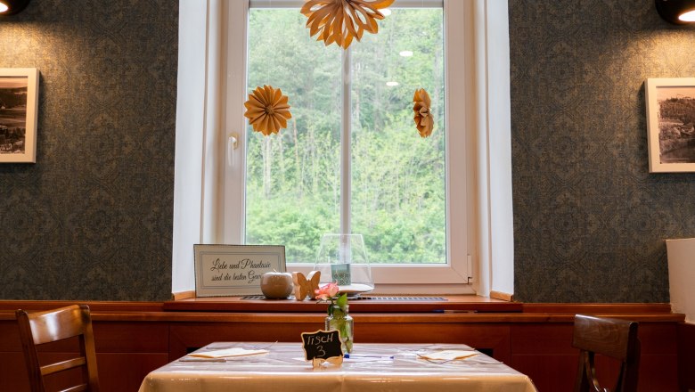 A table in a restaurant with a window view, decorated with paper flowers and a sign saying 'Love and imagination are the best spices'.