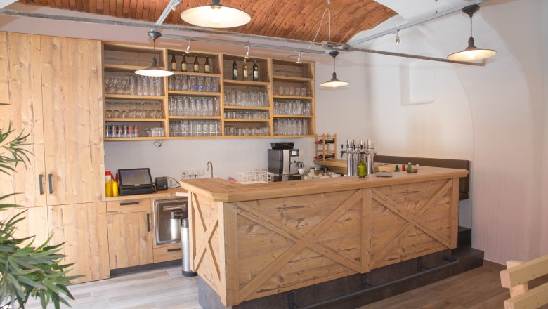 Schank aus Holz mit Gläsern und Flaschen und Backsteindecke.