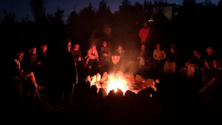 Menschen sitzen im Kreis um ein Lagerfeuer in der Nacht.