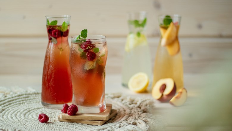 Various glasses of lemonade, decorated with fruit and mint, on a table.