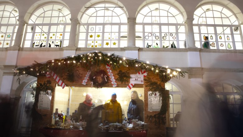 Weihnachtlich dekorierter Punschstand mit Lichtern und Menschen davor, im Hintergrund das Schloss Katzelsdorf