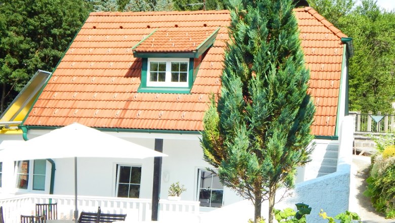 Außenansicht eines weißen Ferienhauses mit rotem Dach und Terrasse.
