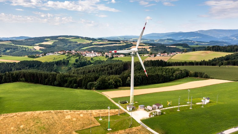 Landschaft mit Windrad und Dorf im Hintergrund.