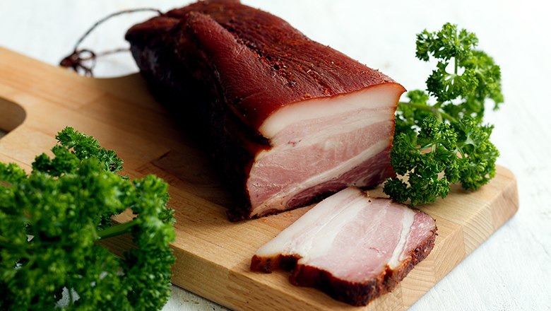 A piece of bacon on a wooden board with parsley.