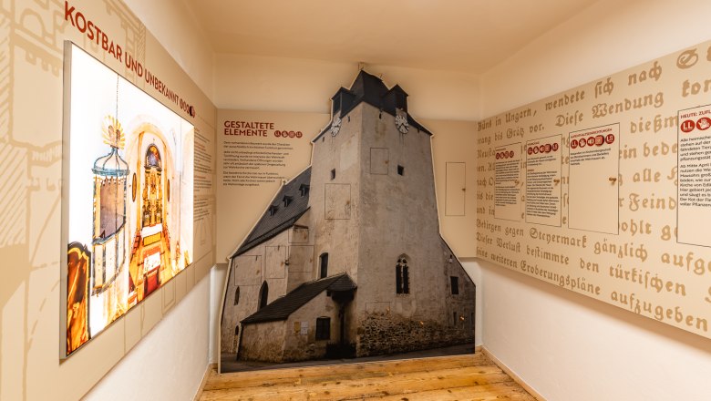 Innenansicht einer Ausstellung über Wehrkirchen mit Texttafeln und einem raumhohen Bild einer Kirche.