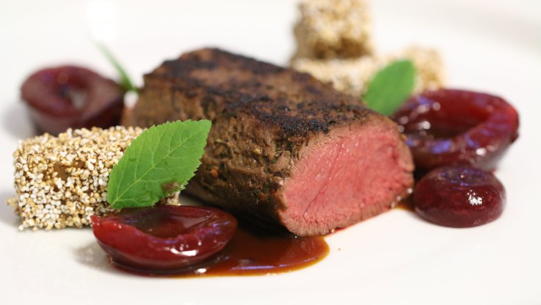Gourmetgericht mit rosa gebratenem Fleisch, Obst und Kr&auml;utern auf einem wei&szlig;en Teller angerichtet.