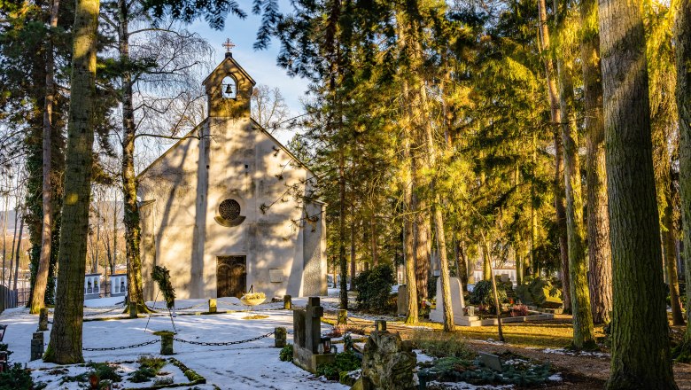 Winterliche Kapelle im Wald mit schneebedecktem Boden und Gräbern.