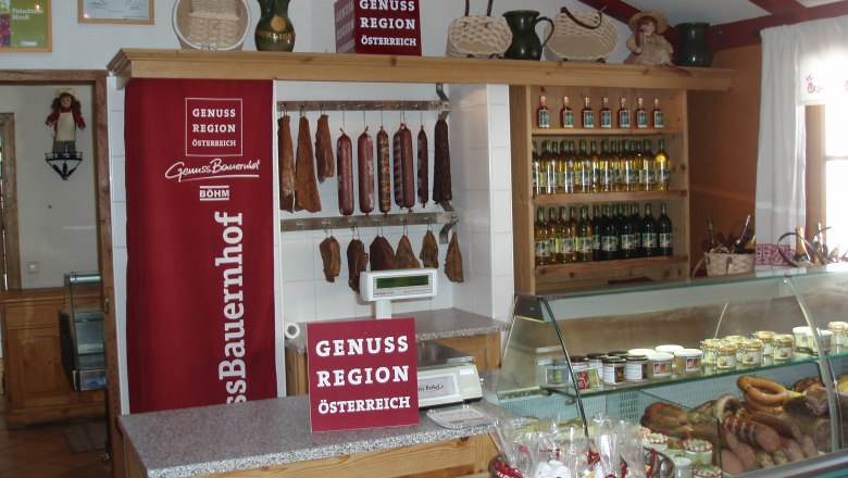 Innenansicht eines Hofladens mit Wurstwaren, Getränken und Dekorationen.