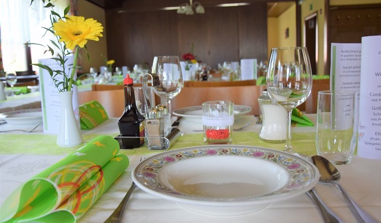 Festlich gedeckter Tisch in einem Saal mit Blumen, Geschirr und Gläsern.