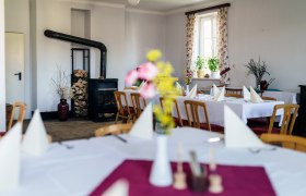 Ein gem&uuml;tlicher Gastraum mit Holzofen, gedeckten Tischen und Blumen auf den Tischen.