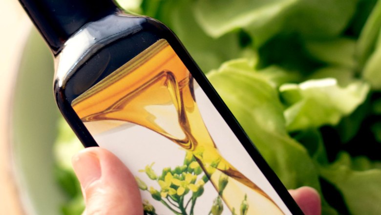 Eine Hand h&auml;lt eine Flasche Bio Leindotter&ouml;l. Im Hintergrund ist eine Sch&uuml;ssel mit gr&uuml;nem Salat.