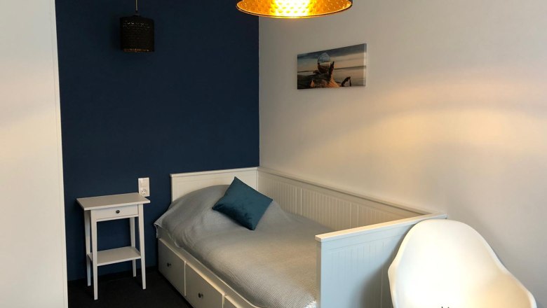 A small, modern single room with a bed, a bedside table and a chair.