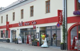 Außenansicht des Koll Bistro Cafés mit rotem Schild und Eisbärfigur mit Eis-Stanizel vor dem Eingang.
