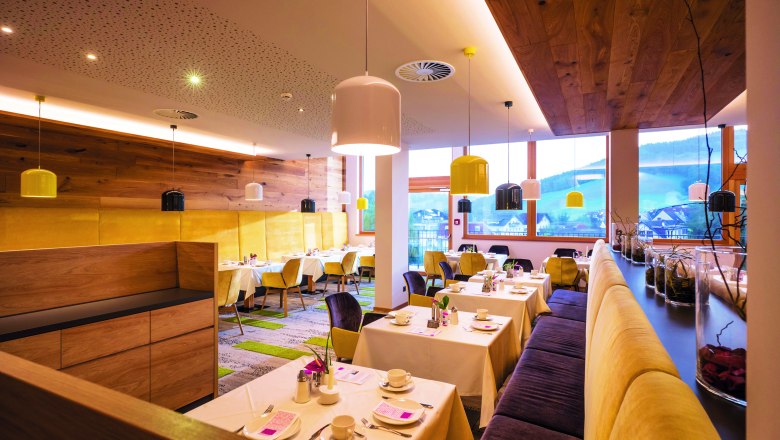 Modernes Restaurant mit Holzwänden, gelben Stühlen und bunten Lampen.