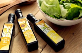 Drei verschiedene &Ouml;le liegen auf einem Holztisch neben einer Sch&uuml;ssel mit gr&uuml;nem Salat.