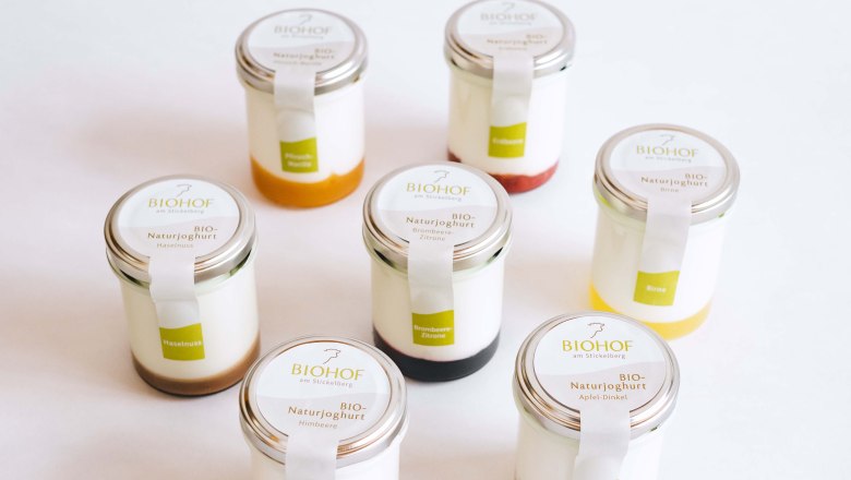 Sieben Gl&auml;ser mit Naturjoghurt, jeweils mit unterschiedlichen Fruchtspiegeln, vor wei&szlig;em Hintergrund.