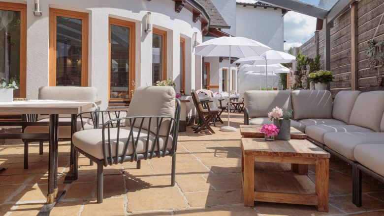 Moderne Terrasse mit bequemen Sitzmöbeln, Holztischen und Sonnenschirmen.