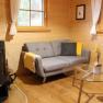 Cozy living room with grey sofa, wooden walls, fireplace and glass table.