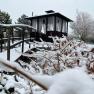 Verschneiter Zen-Garten mit Holzbr&uuml;cke und Pavillon im Hintergrund.