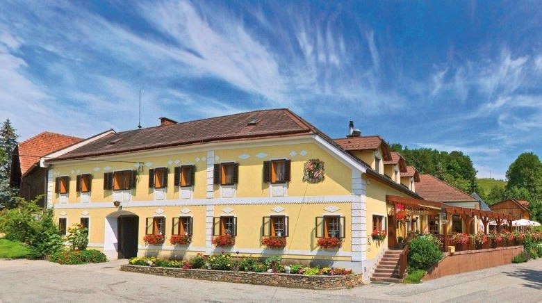 Gasthof Buchegger, © Gasthaus Buchegger, Foto Mayrhofer A. Z. Traditionelles Gasthaus mit gelber Fassade, umgeben von grüner Landschaft und blauem Himmel.