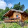 Wooden hut with flowers on the veranda in a green setting.