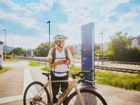 Eine Frau mit Fahrradhelm steht neben einem Fahrrad am Bahnhof in Bad Erlach.
