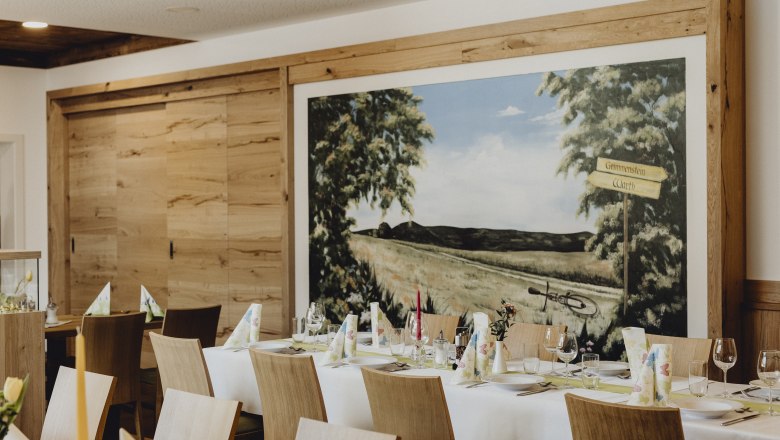 Innenansicht eines Wirtshauses mit gedecktem Tisch und Wandgem&auml;lde.