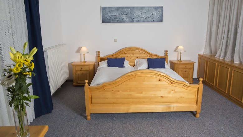 Ein Schlafzimmer mit einem Doppelbett aus Holz, zwei Nachttischen mit Lampen und einem Blumenstrauß auf einem Tisch.