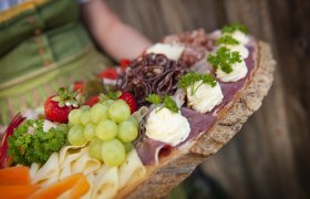 Eine rustikale Platte mit Käse, Schinken, Trauben, Erdbeeren und Kräutern.