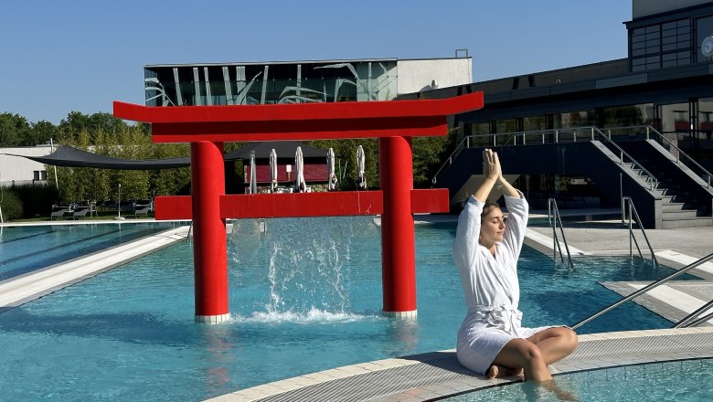 Frau in Bademantel meditiert am Pool vor rotem Torii-Tor.