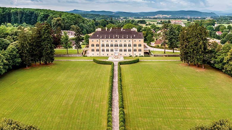 Aerial view of Frohsdorf Castle with its yellow fa&ccedil;ade, long, straight driveway and well-tended park.