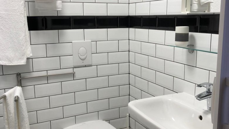 Modernes Badezimmer mit weißen Fliesen, Waschbecken und Toilette.