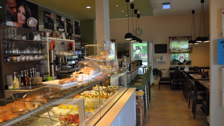 Interior view of a caf&eacute; with counter full of pastries and seating area.