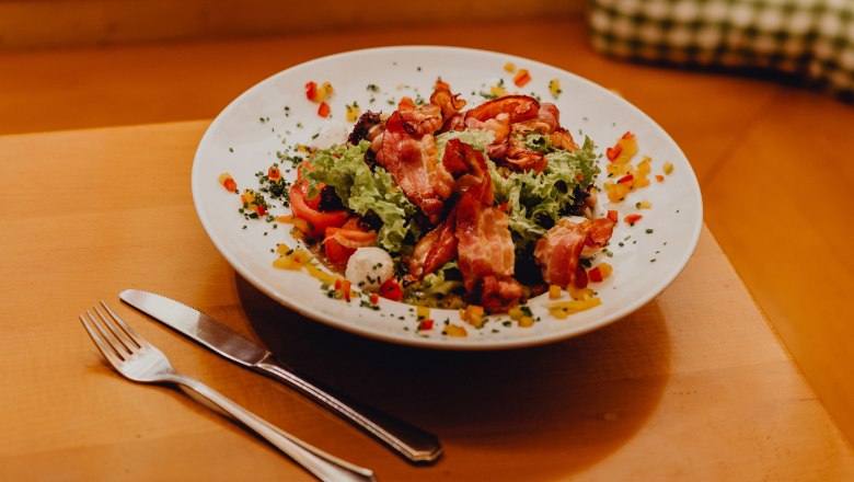Ein Teller mit gemischtem Salat, Ziegenkäse und Speck auf einem Holztisch.