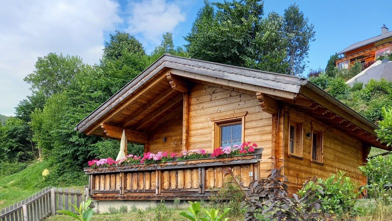 Wooden hut with flowers on the veranda in a green setting.