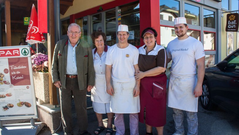 Fünf Personen stehen lächelnd vor einem Geschäftseingang.