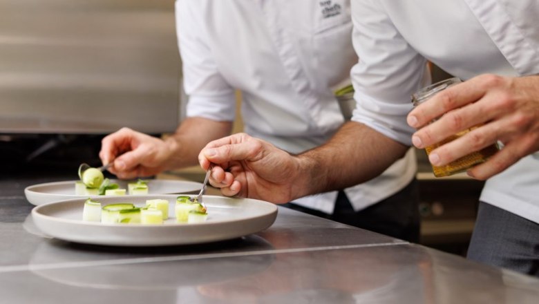 Zwei K&ouml;che in wei&szlig;en Kochjacken richten Gourmetgerichte auf wei&szlig;en Tellern an.
