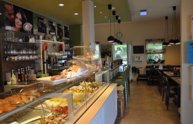 Innenansicht eines Cafés mit Theke voller Gebäck und Sitzbereich.