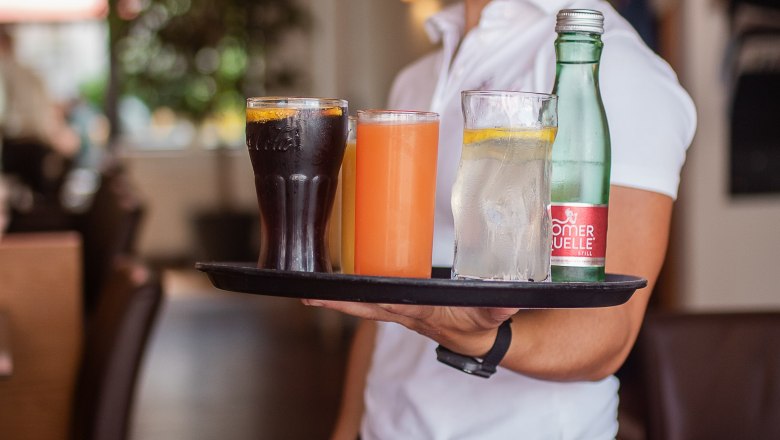 A smiling waitress in a restaurant carries a tray with various drinks.