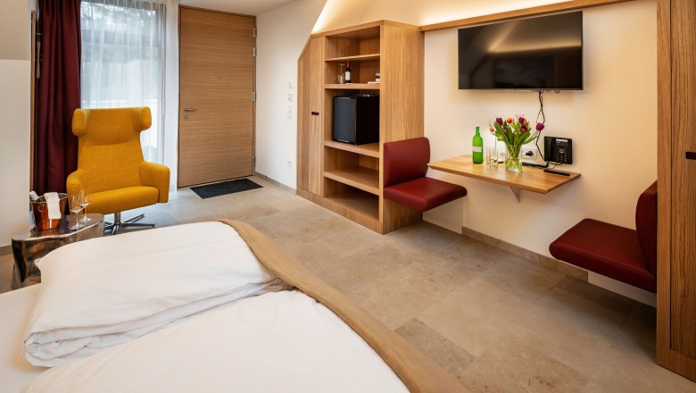 Modern eingerichtetes Hotelzimmer mit gelbem Sessel, Holzm&ouml;beln und Blumen auf einem Tisch.