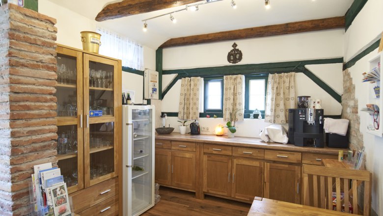 A cozy breakfast room with wooden furniture, a fridge, a coffee machine and decorative wooden beams on the ceiling.