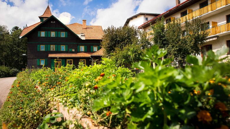 Ein traditionelles Gebäude mit grünem Fensterladen und einem Garten im Vordergrund unter blauem Himmel.